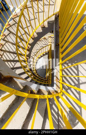 Vista dall'alto di una scala a chiocciola in cemento con ringhiere gialle in una mattinata soleggiata Foto Stock