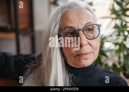 Ritratto di donna anziana penitente seduta in casa. Foto Stock