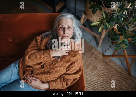 Ritratto di donna anziana penitente seduta in casa. Foto Stock