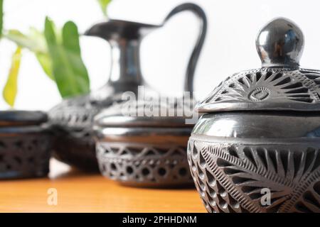 Artigianato tipico messicano. Set di vasi di argilla nera fatti a mano a Oaxaca, Messico. Fondo bianco, base in legno e pianta sullo sfondo. Foto Stock