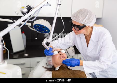 Cosmetologo che usa il laser per rifare la pelle del volto della donna matura Foto Stock