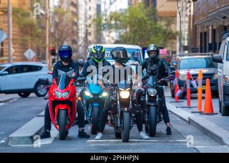 Quattro motociclisti che indossano caschi a faccia intera, si fermandono a un incrocio a Pitt Street, Sydney, Australia Foto Stock