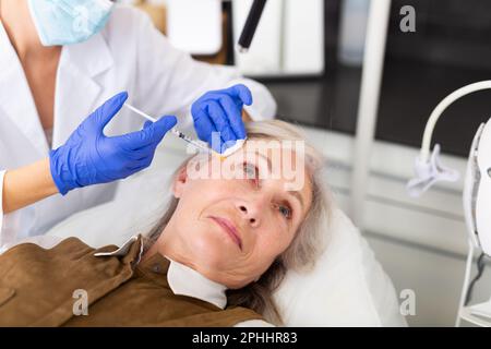 Donna anziana che riceve la botulinoterapia per il suo viso Foto Stock