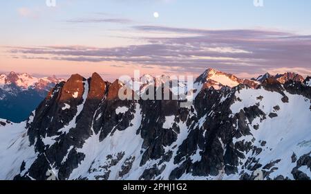La Luna piena è sospesa nel cielo mentre il tramonto illumina le Montagne Rocciose dello splendido North Cascades National Park di Washington. Foto Stock