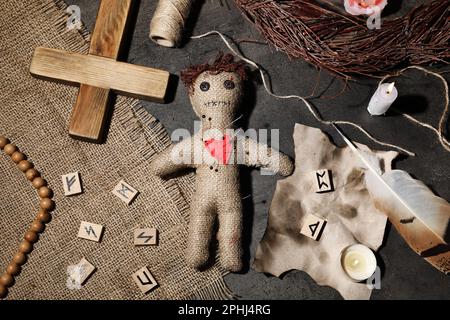 Voodoo bambola trafitto con spilli e oggetti cerimoniali su tavolo grigio, piatto Foto Stock