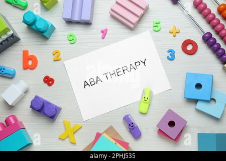 Composizione piatta con frase ABA Therapy e giocattoli colorati su tavolo di legno bianco Foto Stock