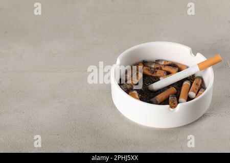 Posacenere in ceramica bianca con mozziconi di sigaretta sul tavolo grigio. Spazio per il testo Foto Stock