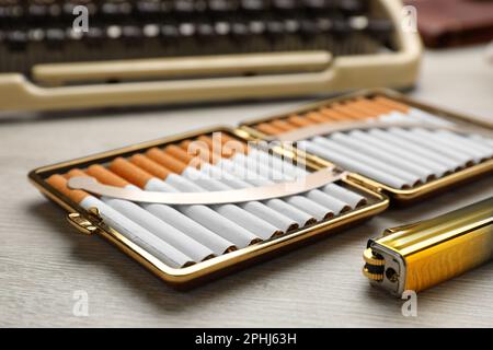 Cassa aperta con sigarette filtro tabacco e accendino vicino a macchina da scrivere vintage su tavolo di legno, primo piano Foto Stock