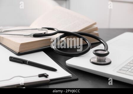 Apri il libro di testo, gli appunti e lo stetoscopio degli studenti vicino al notebook su un tavolo grigio all'interno, primo piano. Educazione medica Foto Stock