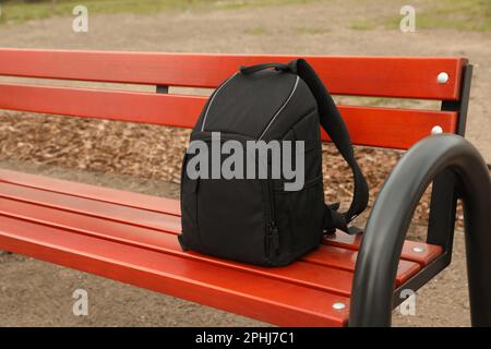 Elegante zaino nero per fotocamera su banco in legno all'aperto Foto Stock