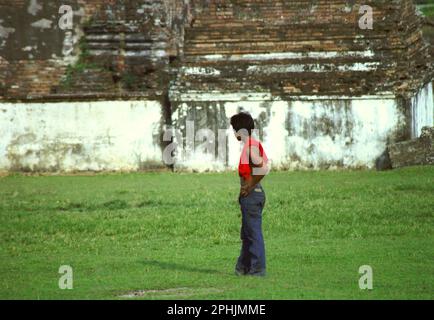 Un giovane è in piedi sul prato in uno sfondo di un muro al resto del palazzo Kaibon, uno dei beni culturali del periodo Sultanato Banten situato in zona ora chiamato Banten lama (Old Banten) a Serang, Banten, Indonesia. "La sostenibilità del patrimonio culturale è fortemente legata all'effettiva partecipazione delle comunità locali alla conservazione e alla gestione di queste risorse", secondo un team di scienziati guidati da Sunday Oladipo Oladeji nel loro articolo di ricerca pubblicato su Sage Journals il 28 ottobre 2022. Foto Stock