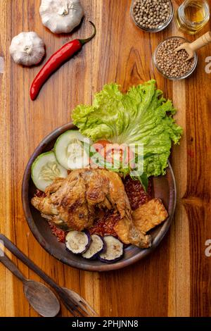 Pollo fritto croccante con salsa piccante al peperoncino o sambal in piatto di ceramica su tavolo di legno Foto Stock