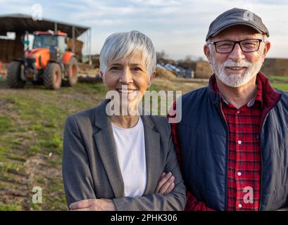 Ritratto di coppia contadina matura in piedi di fronte al trattore sul ranch del bestiame Foto Stock