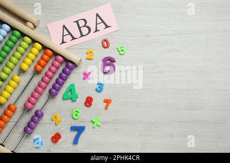 Foglio di carta con abbreviazione ABA (Applied Behavior Analysis), abacus e numeri colorati su tavola di legno bianco, piano. Spazio per il testo Foto Stock