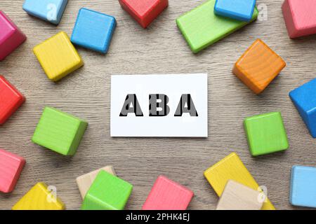 Blocchi da costruzione colorati e scheda con l'abbreviazione ABA su tavolo di legno, piatto Foto Stock