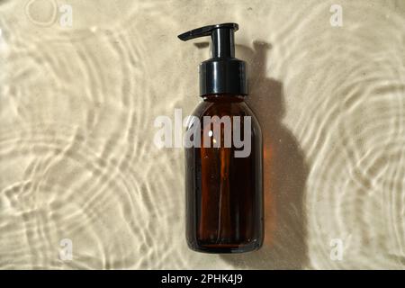 Bottiglia di olio idrofilo in acqua su sfondo beige, vista dall'alto Foto Stock