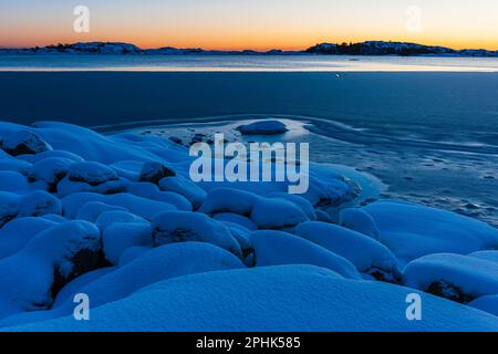 Uno splendido tramonto invernale illumina il tranquillo mare ghiacciato e la terra innevata della Svezia, mostrando la bellezza della natura. Foto Stock