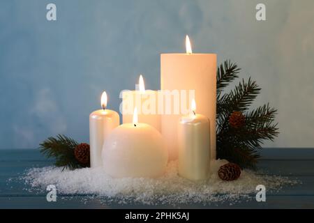 Candele bruciate con ramo di abete, coni e neve artificiale su tavola di legno blu. Atmosfera natalizia Foto Stock