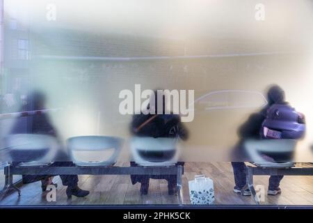 Tre persone sedute in una sala d'attesa, viste attraverso vetro traslucido. Bruxelles. Foto Stock
