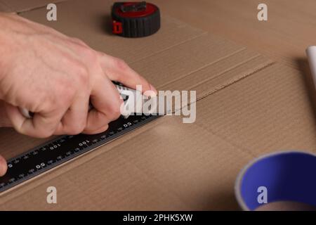 Uomo che taglia cartone con coltello e righello, primo piano Foto Stock