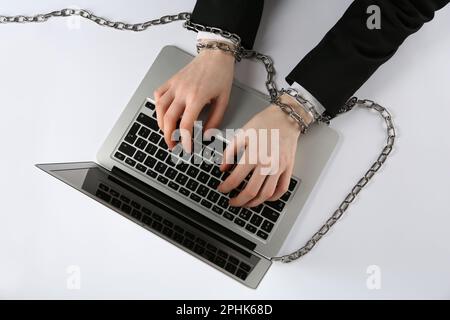 Uomo con mani incatenate che digita sul notebook su sfondo bianco, vista dall'alto. Dipendenza da Internet Foto Stock