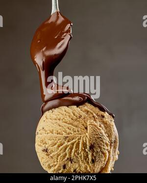salsa di cioccolato fuso che scorre su palla di gelato al caramello su sfondo grigio Foto Stock