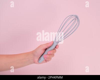 Primo piano della frusta in plastica che tiene la mano isolata su sfondo rosa. Utensile da cucina per montare panna o uova. Foto Stock