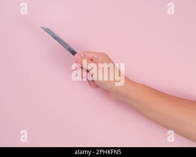 Primo piano della lama femmina per tenere la mano isolata su sfondo rosa. Mano che tiene una taglierina d'argento con una lama affilata in primo piano. Foto Stock