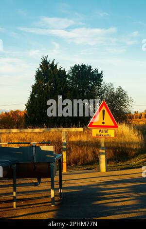 Un cartello, condizioni scivolose in lingua finlandese nel luogo di pulizia dei tappeti al tramonto . Segnalazione di condizioni scivolose. Foto Stock