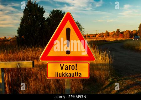 Un cartello, condizioni scivolose in lingua finlandese nel luogo di pulizia dei tappeti al tramonto . Segnalazione di condizioni scivolose. Foto Stock