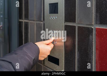 Sistema di casa sicuro, pressione della mano sulla tastiera dell'interfono, utilizzo di telefono della porta, telefono della porta, telefono dell'entryphone, chiamata videofoniera, Campanello elettronico digitale Foto Stock