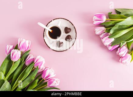 tulipani lilla primaverili e una tazza di caffè aromatico su un piattino con cioccolatini a forma di cuore. sfondo festivo. una copia dello spazio Foto Stock