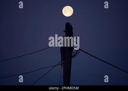 Una luna piena di neve sta ambientando sopra la mia casa in Radley Village. Snow Moon è il nome convenzionale per la luna piena di febbraio. Foto Stock