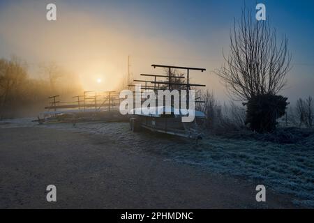 Un'alba invernale misteriosa e sorprendentemente bella scoppia da dietro gli alberi sulle rive del Tamigi da Radley College Boathouse su un Wi ghiacciato Foto Stock