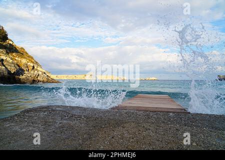 Spiaggia su un mare con un ragnatela e le onde, l'acqua spruzza verso l'alto. Strand am Meer mit einem Steg und Wellen. Das wasser spritz nach oben. Foto Stock