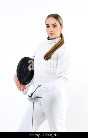 Ragazza reccatore con una spada su uno sfondo bianco. Ritratto di una ragazza in costume da scherma con maschera e spada. Foto Stock