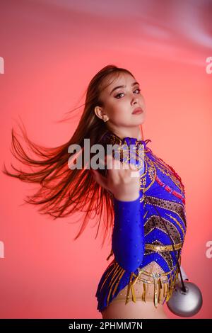 Ragazza ginnastica indossa un leotard ginnico tenendo una spada nelle mani su uno sfondo rosa. Foto Stock