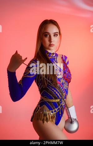 Ragazza ginnastica indossa un leotard ginnico tenendo una spada nelle mani su uno sfondo rosa. Foto Stock