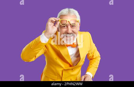 Ragazzo allegro e positivo con barba grigia sorridente, alzando gli occhiali dagli occhi vestiti di tuta gialla Foto Stock