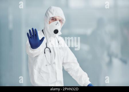 Mostra il movimento di arresto manuale. Medico scienziato maschile in camice da laboratorio, occhiali difensivi e maschera Foto Stock