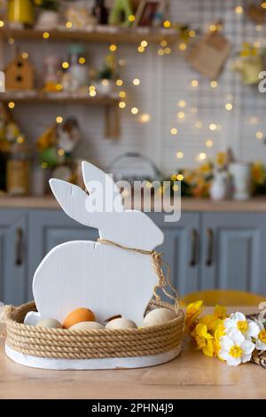 Un cesto con un coniglio bianco di legno e uova naturali si trova sul tavolo in cucina Foto Stock