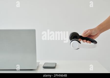 Mano dell'uomo d'affari che mette le cuffie sulla scrivania dell'ufficio con il laptop e lo smartphone Foto Stock