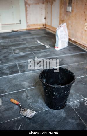 Installatori di cucina: Piastrelle di pietra pavimento. Secchio, acqua, trota e grota. Attrezzi del mestiere per la posa di un nuovo pavimento in ardesia. Da una serie di immagini correlate. Foto Stock