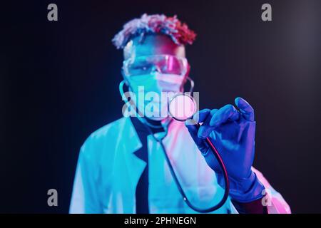 Medico intelligente in stetoscopio protettivo uniforme. Illuminazione futuristica al neon. Giovane afro-americano in studio Foto Stock