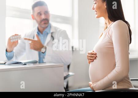 Gravidanza e concetto di medicina. Ginecologo maschio che dà pillole alla donna incinta durante l'appuntamento in ospedale Foto Stock