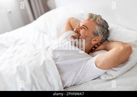 Uomo di mezza età, riposato e felice, che si rilassa a letto Foto Stock