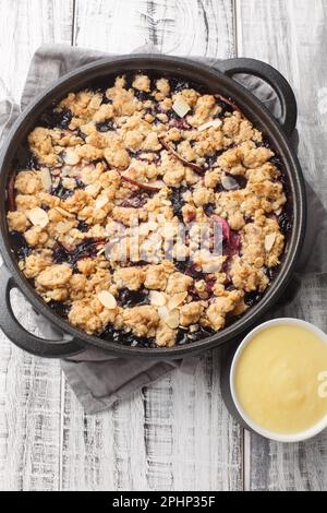 Deliziosa torta estiva di frutti di bosco al forno con mele e mirtilli serviti con salsa alla vaniglia in primo piano sul tavolo. Vista verticale dall'alto Foto Stock