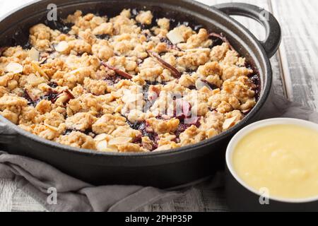 Torta Smulpaj Svedese crumble con mele e mirtilli serviti con salsa alla vaniglia fatta in casa closeup sul tavolo di legno. Orizzontale Foto Stock