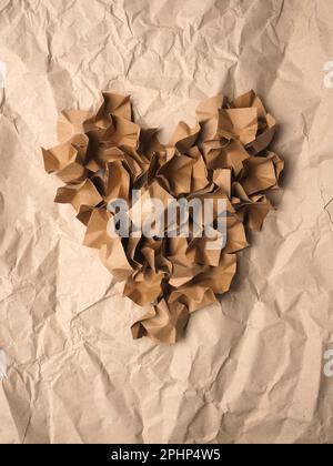 Forma del cuore realizzata con materiale di imballaggio in carta riciclata su uno sfondo di carta riciclata schiacciata Foto Stock