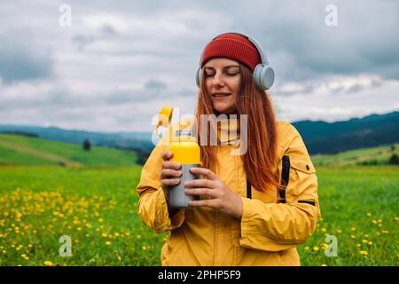 Felice viaggiatore giovane donna che riposa in montagna e beve il tè dai thermos al tramonto in primavera o stagione estiva. Foto Stock